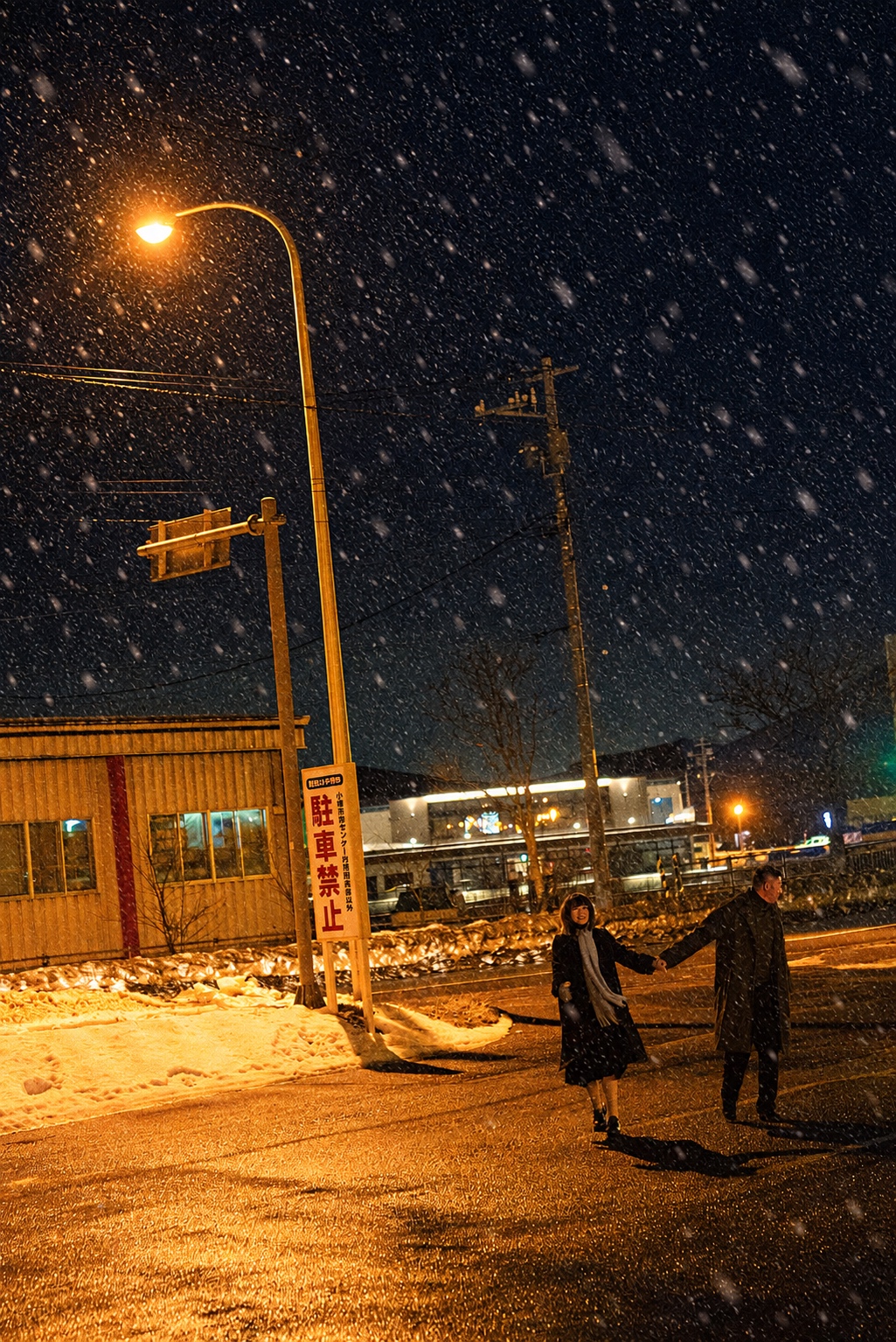 橙色路灯照着雪地，两个人远远牵手站在街边